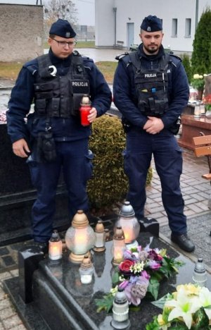 Dwóch policjantów w mundurach stoi przy grobie.