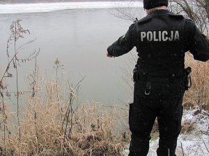 Policjant w mundurze stoi nad brzegiem częściowo zamarźniętego jeziora.