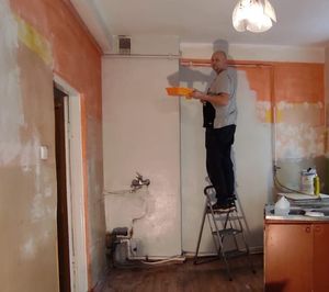 Mężczyzna na drabinie maluje ścianę w pokoju.