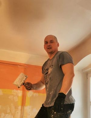 Mężczyzna na drabinie maluje sufit w pomieszczeniu.