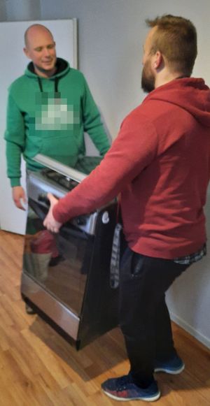 Dwóch mężczyzn wnosi kuchenkę gazową do pomieszczenia.