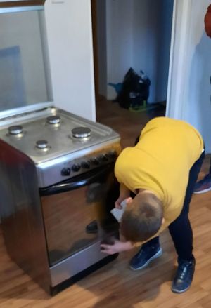 Młody chłopiec wyciera dół kuchenki gazowej ściereczką.