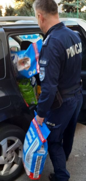 Policjant w mundurze wkłada worki z karmą do cywilnego auta.