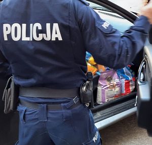 Policjant w mundurze wkłada paczki z karmą do cywilnego auta.