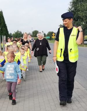 Policjantka w mundurze prowadzi dzieci z przedszkola na chodniku.