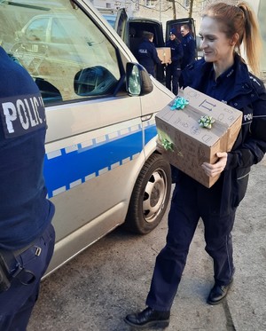 Policjantka w mundurze niesie karton do radiowozu.