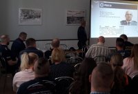 Umundurowany policjant na prezentacji multimedialnej prezentuje sylwetkę dzielnicowego gminy Namysłów uczestnikom spotkania.