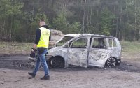 Technik kryminalistyki wykonuje oględziny wraku spalonego auta.