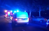 Radiowóz i wóz strażacki z włączoną sygnalizacją świetlną w nocy stoją na drodze. Obok samochód osobowy w rowie.