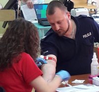 Mężczyzna ubrany w mundur policyjny oddaje krew w obecności pielęgniarki w czerwonym kitlu.