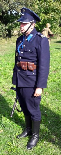 Mężczyzna przebrany w mundur policyjny z 1939 roku stoi na trawie.