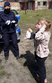 Policjantka w mundurze przekazuje maseczki ochronne dla dzieci.