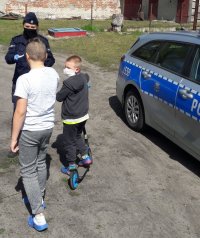 Policjantak w mundurze przekazuje maseczki dzieciom.
