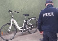 Mężczyzna w policyjnym mundurze spogląda na rower oparty o ściane.