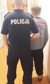 Dwóch mężczyzn stoi na korytarzu, jedn ma na sobie mundur policyjny.