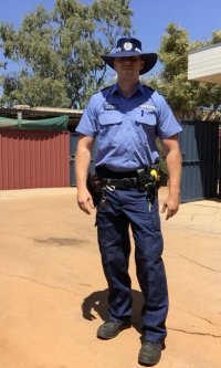 Mężczyzna w australijskim policyjnym mundurze stoi na piasku.