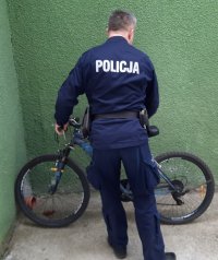 Policjant w granatowym mundurze stoi przy rowerze górskim.