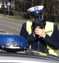 Policjant w mundurze mierzy prędkość przejeżdżających samochodów.