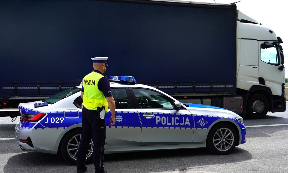zdjęcie: policjant drogówki stojący obok radiowozu i ciężarówki
