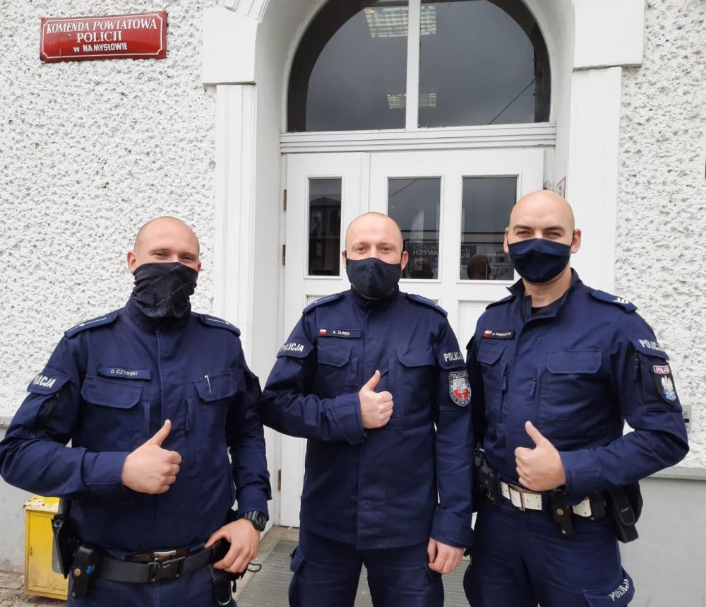 trzej policjanci z maseczkami na twarze stoją naprzeciwko budynku komendy policji