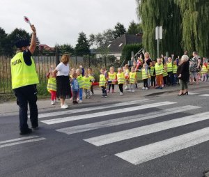 Policjantka w mundurze przeprowadza dzieci przez jezdnię.