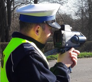 Policjant w mundurze mierzy prędkość kierowcom za pomocą ręcznego miernika prędkości.