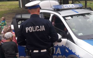 Policjant w mundurze stoi przy radiowozie, do którego wsiadają dzieci.