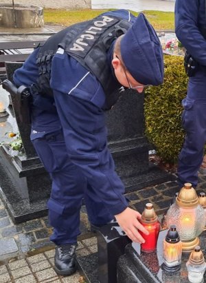 Policjant w mundurze policyjnym kładzie na grobie czerwony znicz.