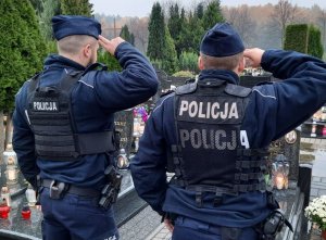 Dwóch policjantów w mundurach salutuje przy grobach.