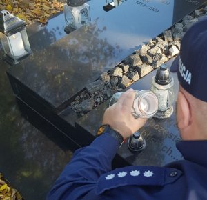 Policjant zapala znicz przy grobie.