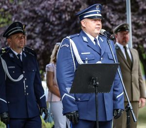 Mężczyzna w galowym, policyjnym mundurze stoi przy pulpicie i przemawia do mikrofonu.