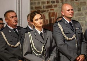 Policjantka i dwóch policjantów stoją w kościelnej ławce w policyjnych mundurach.