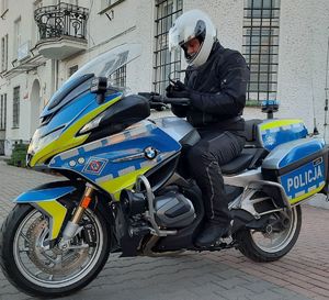 Policjant w mundurze siedzi na nowoczesnym oznakowanym policyjnym motorze.