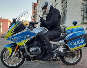 Policjant siedzi na siedzisku motocykla policyjnego oznakowanego.