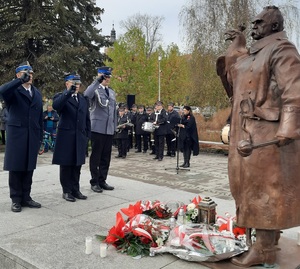 Trzech mężczyzn w mundurach salutuje przed pomnikiem Józefa Piłsudskiego.