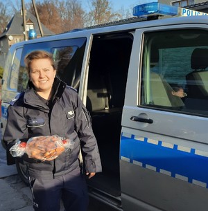 Policjantka w mundurze stoi przy radiowozie a w ręku trzyma paczkę pierników.