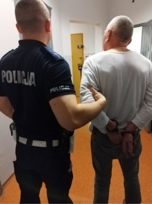 Umundurowany policjant trzyma zatrzymanego mężczyznę za rękę.