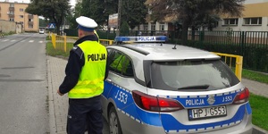 policjant stojąc obok radiowozu obserwuje przejście dla pieszych