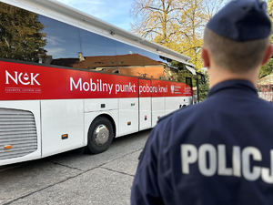 Zdjęcie przedstawia policjanta stojącego przed krwiobusem.