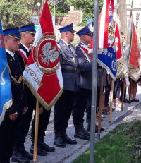 Poczty sztandarowe straży pożarnej i policji stoją w rzędzie na baczność.