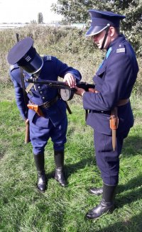 Mężczyźni przebrani w policyjne mundury z 1939 roku doglądają pistletu maszynowego.