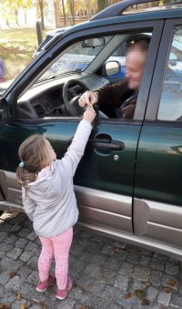 Mała dziewczynka podaje plaster cytryny dla kierowcy siedzącego w aucie.