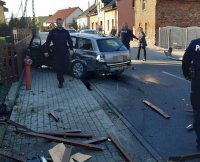 Mężczyzna w policyjnym mundurze idzie chodnikiem a za nim rozbity samochód.