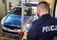 Policjant w mundurze stoi przy oznakowanym radiowozie i urządzeniu pomiarowym do świateł.