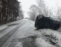 Samochód osobowy leży na prawym boku przy ośnieżonej drodze.