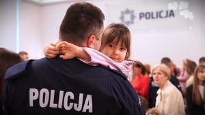 Zdjęcie przedstawia dziewczynkę na rękach policjanta.